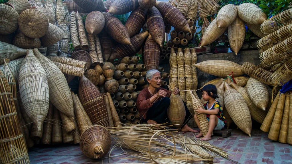 View of an old lady with a kid teaching how to weave bamboo baskets.