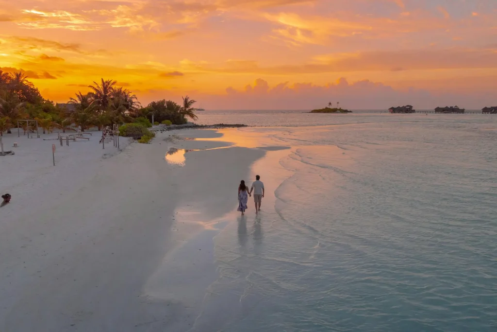 a couple walking at the beach during a sunset.