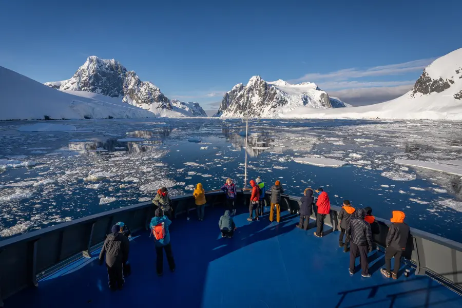 Travellers on expedition ship deck viewing Antarctic landscape.