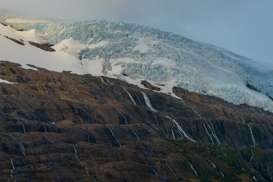 Glacier flowing over rocky Antarctic coastline.