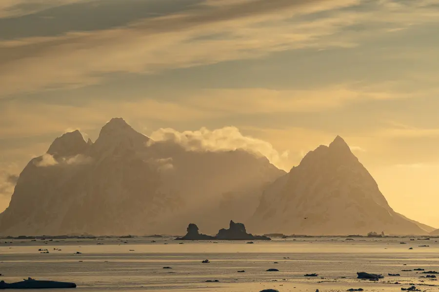 View of Antarctic mountains and icebergs during sunset.