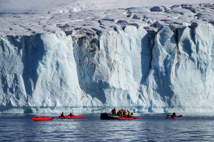 View of Kayakers and Zodiac boat near Antarctic glacier wall.